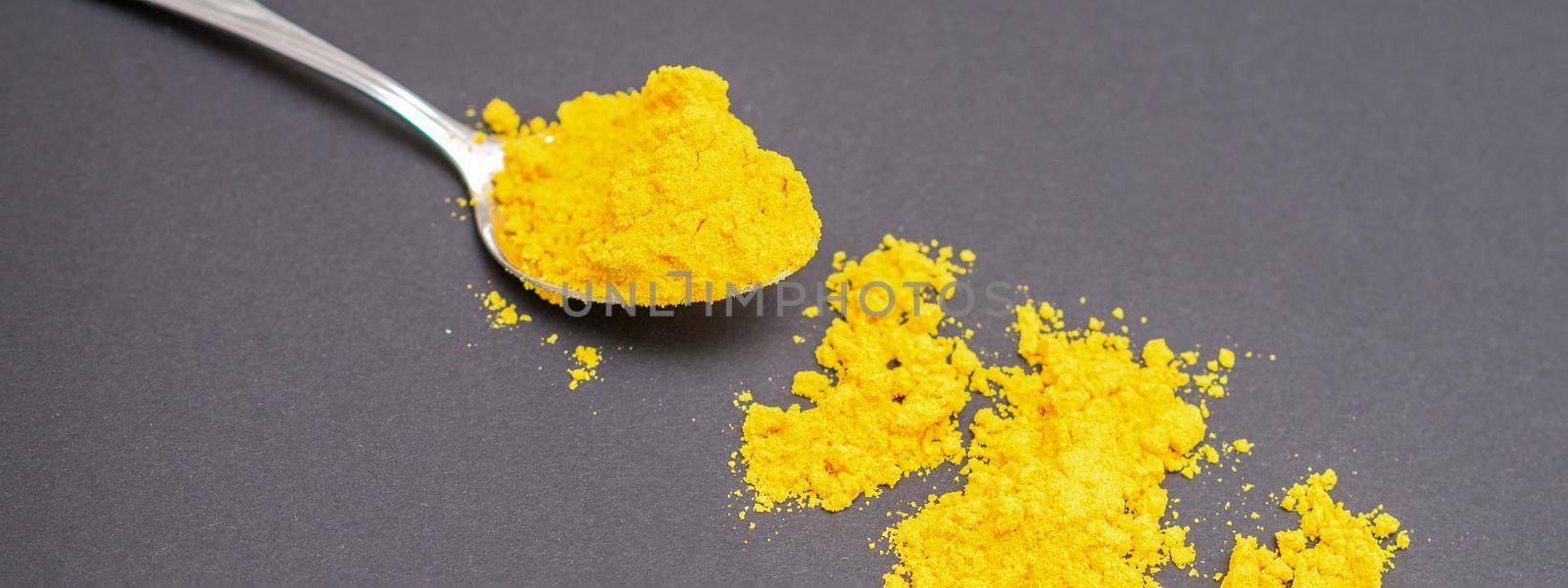 Turmeric or curcuma powder on metal spoon and scattered on dark background.