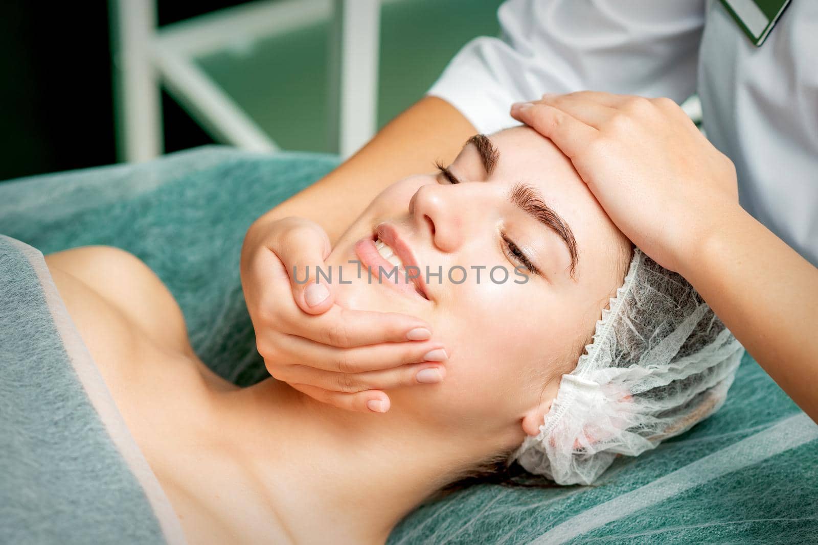 Young woman getting facial massage with closed eyes by beautician in beauty salon