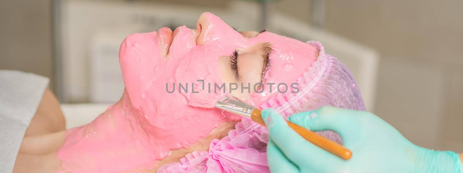 Cosmetologist applying pink alginic mask by okskukuruza