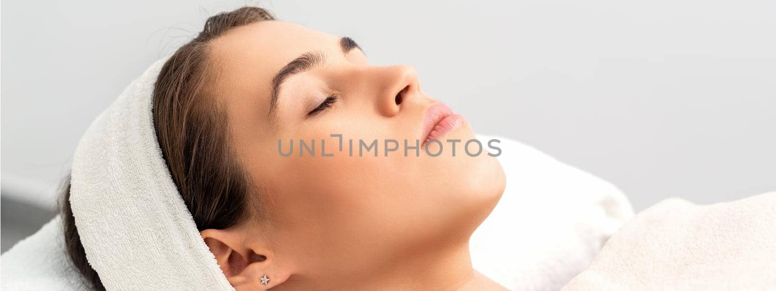 Side view of young woman lying on beautician table with closed eyes while waiting for cosmetic procedure in beauty salon