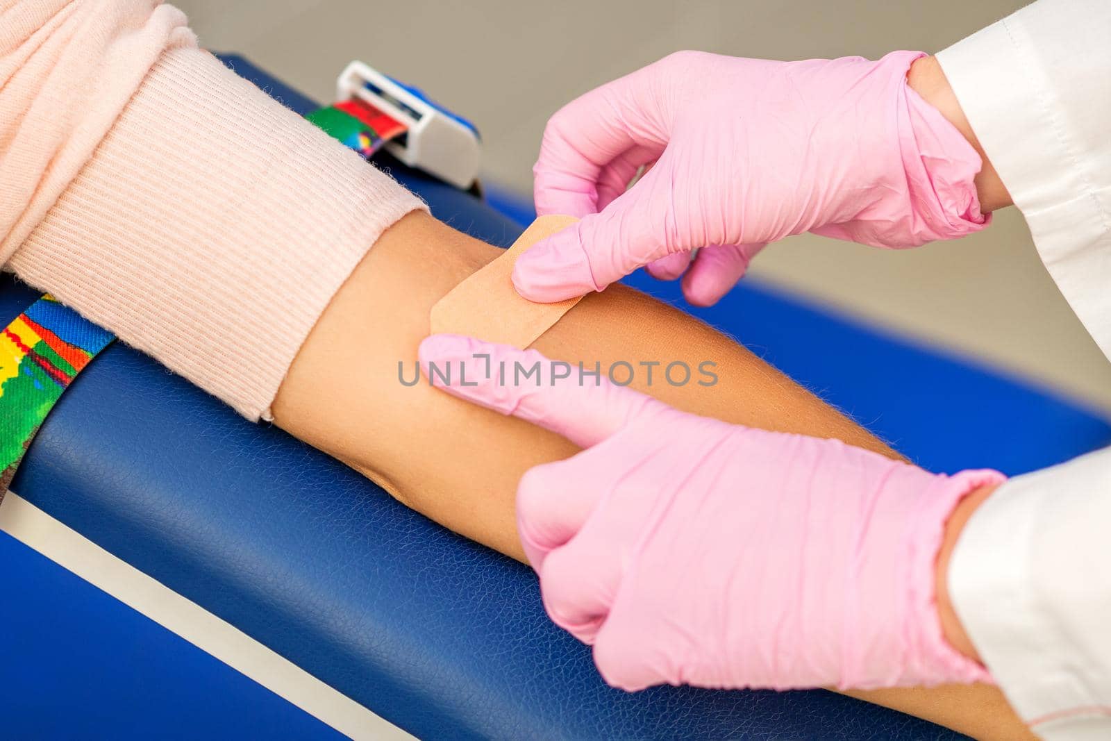 Close up of nurse hand applying adhesive plaster on arm of patient after blood collection in the hospital