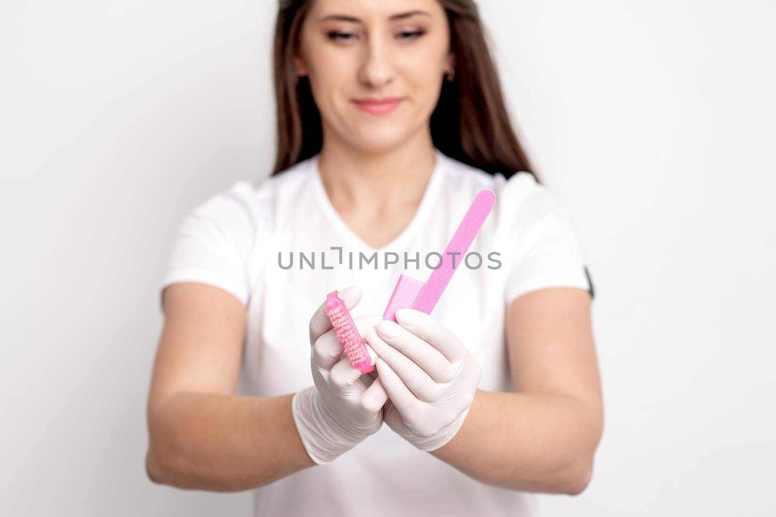 Manicure tools in hands of young female manicure master on white background. Selective focus