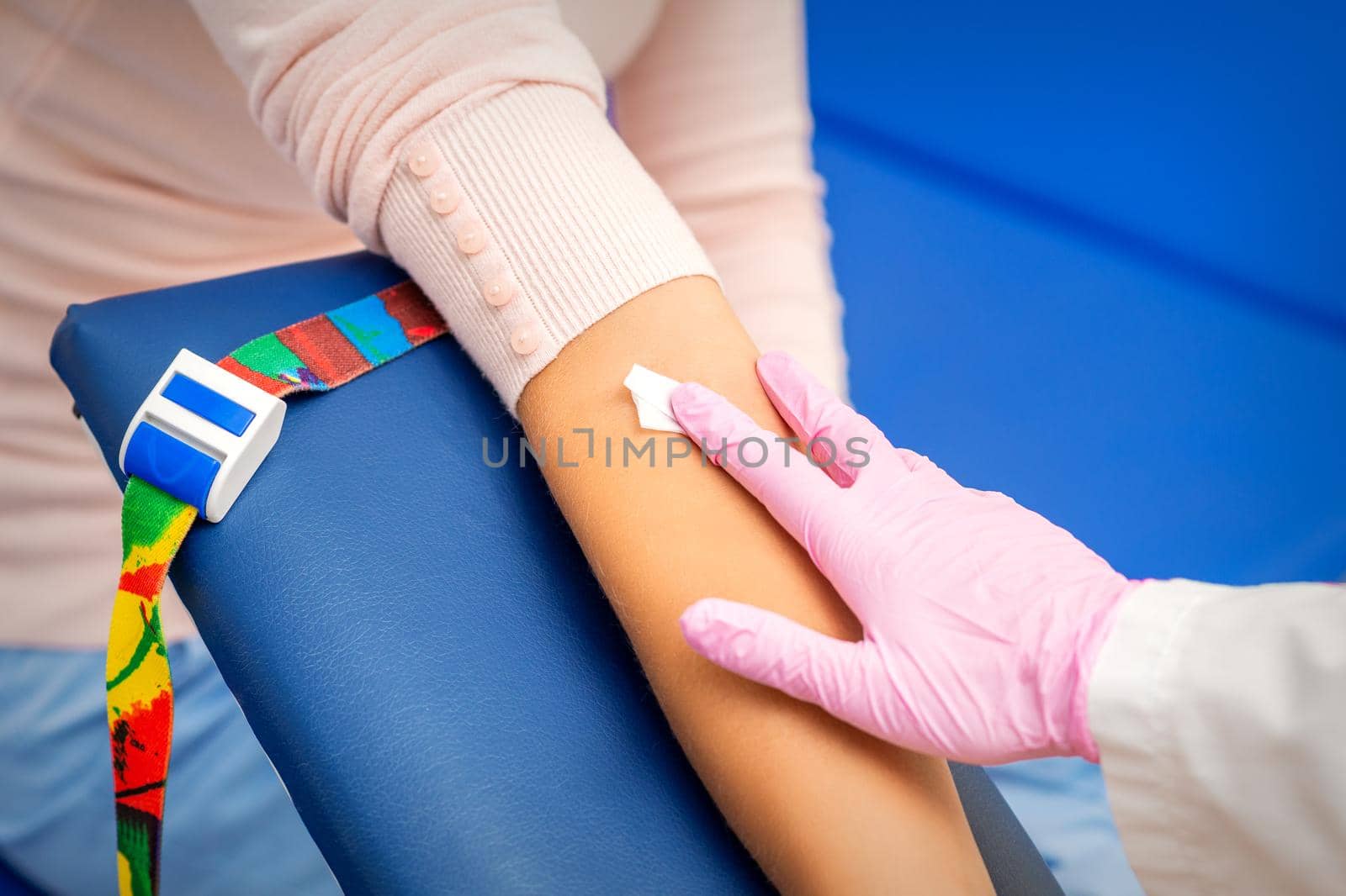 Hand of nurse applying cotton swab to arm of young woman after blood sample in the hospital