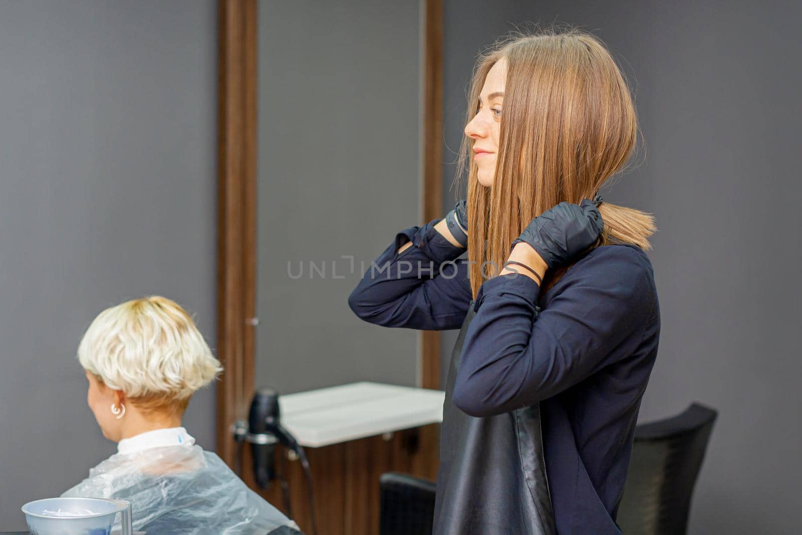 Female hairdresser puts on black apron before cutting the client's hair