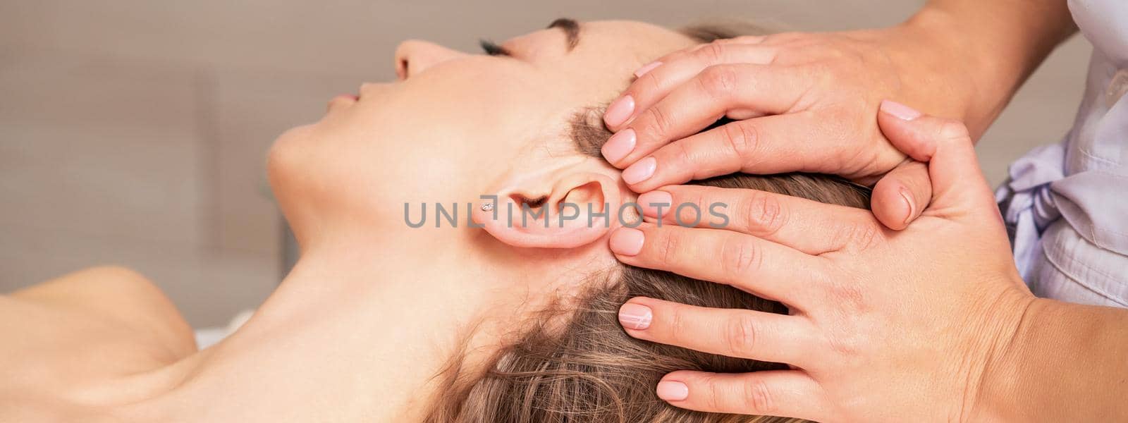 Young woman receiving head massage by hands of beautician in spa beauty center
