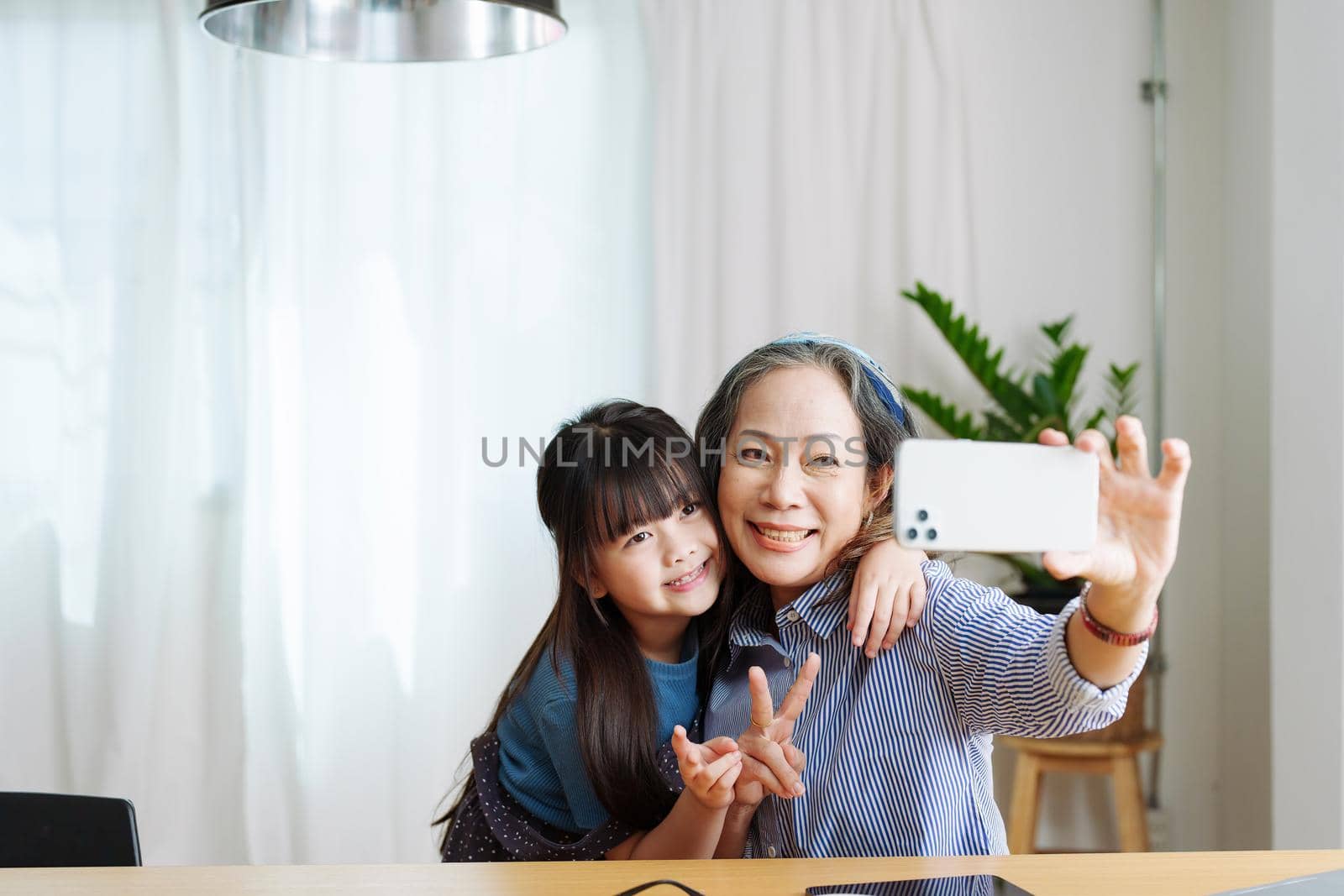 Asian portrait, grandma and granddaughter doing recreational activities using their phones to take selfies happily by Manastrong