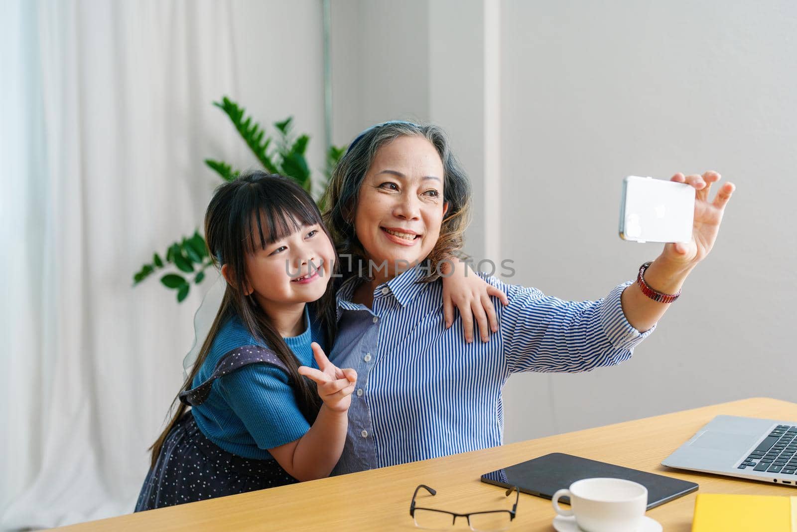 Asian portrait, grandma and granddaughter doing recreational activities using their phones to take selfies happily.