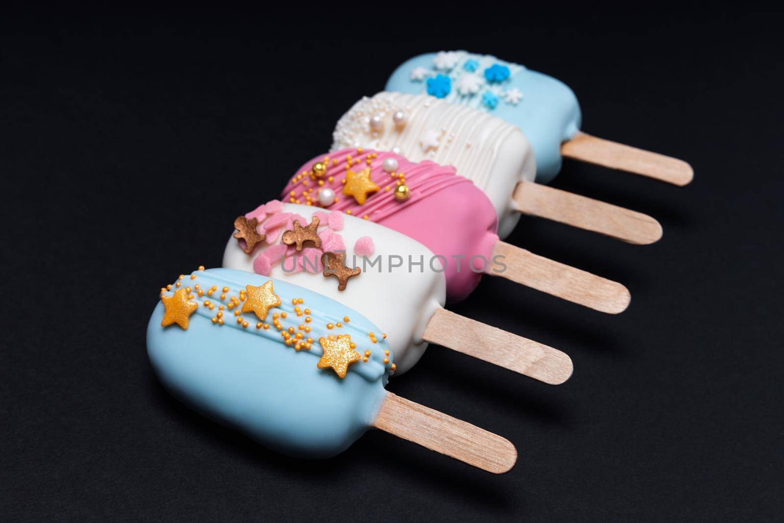 Five decorated cake pops ice creams in a row on black background