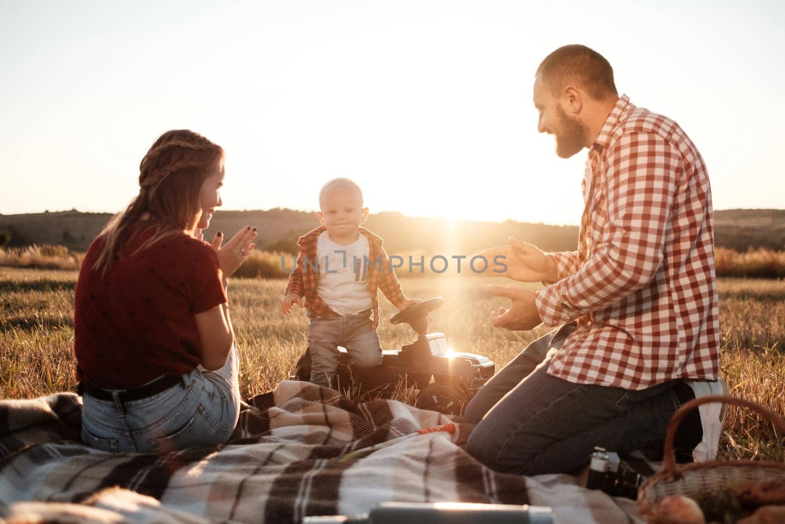 Happy Young Family Mom and Dad with Their Little Son Enjoying Summer Weekend Picnic Outside City in the Field at Sunny Day Sunset, Vacation Time Concept