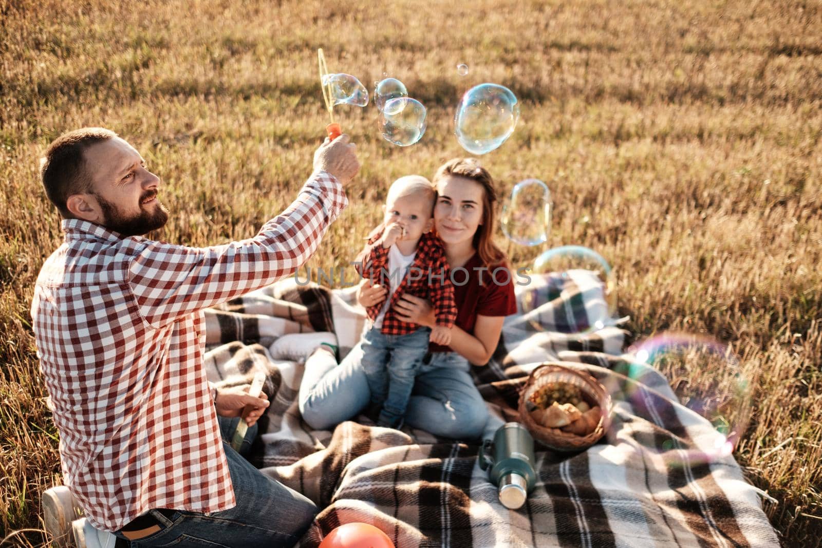 Happy Young Family Mom and Dad with Their Little Son Enjoying Summer Weekend Picnic Outside the City in Field at Sunny Day Sunset, Vacation Time Concept