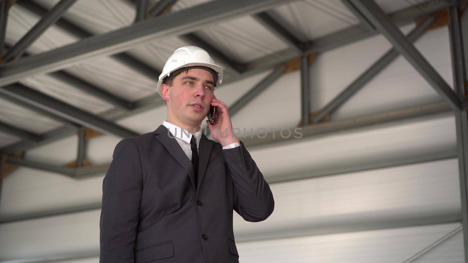 A young man in a helmet speaks on the phone at a construction site. The boss in a suit is talking on the phone. 4k