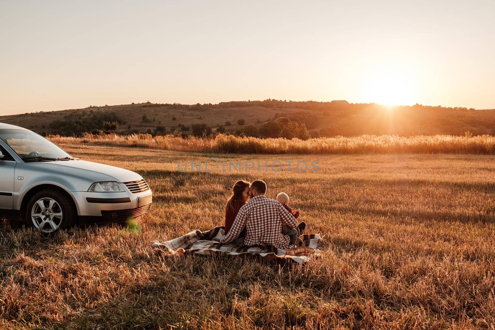Happy Young Family Mom and Dad with Their Little Son Enjoying Summer Weekend Picnic on the Car Outside the City in Field at Sunny Day Sunset, Vacation and Road Trip Concept