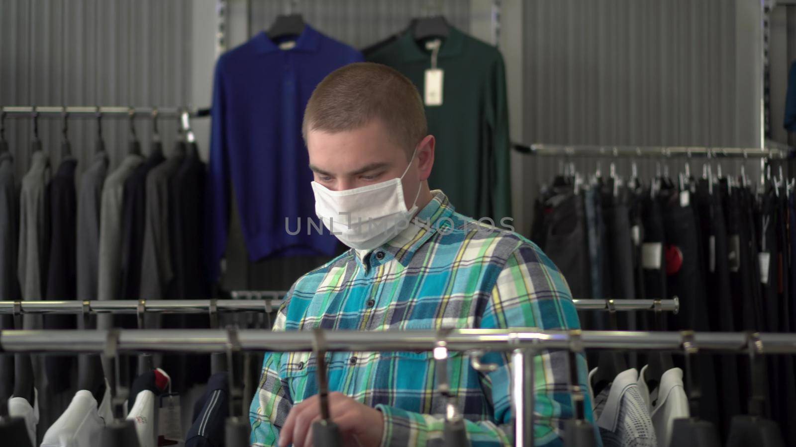 A young man in a medical mask is choosing clothes in a store. Clothing store. 4k