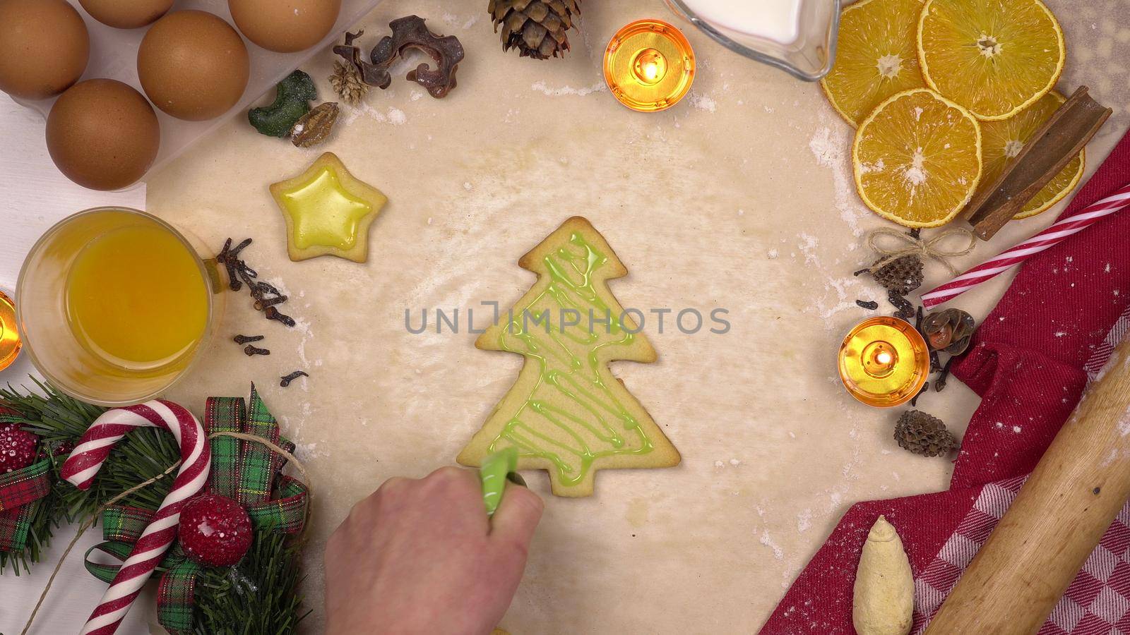 A young woman decorates a festive Christmas cookie in the form of a Christmas tree with colored icing. View from above. 4k
