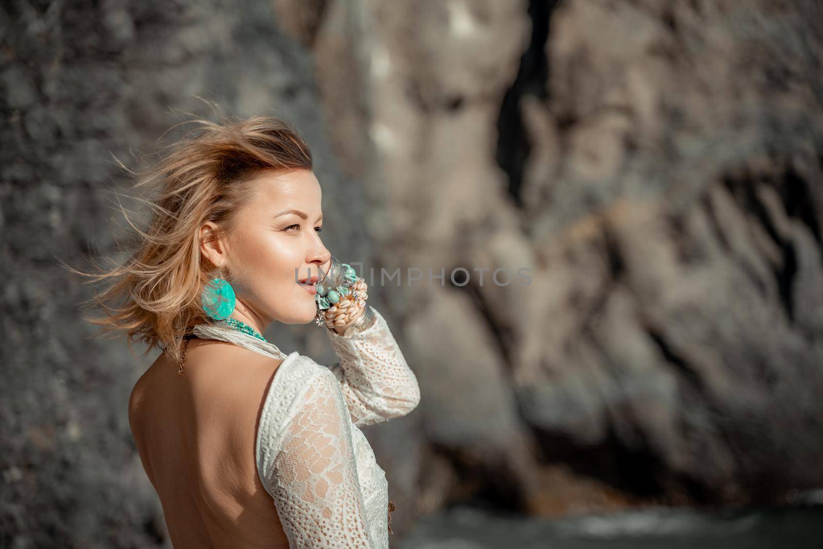 Middle aged woman looks good with blond hair, boho style in white long dress on the beach decorations on her neck and arms. by Matiunina