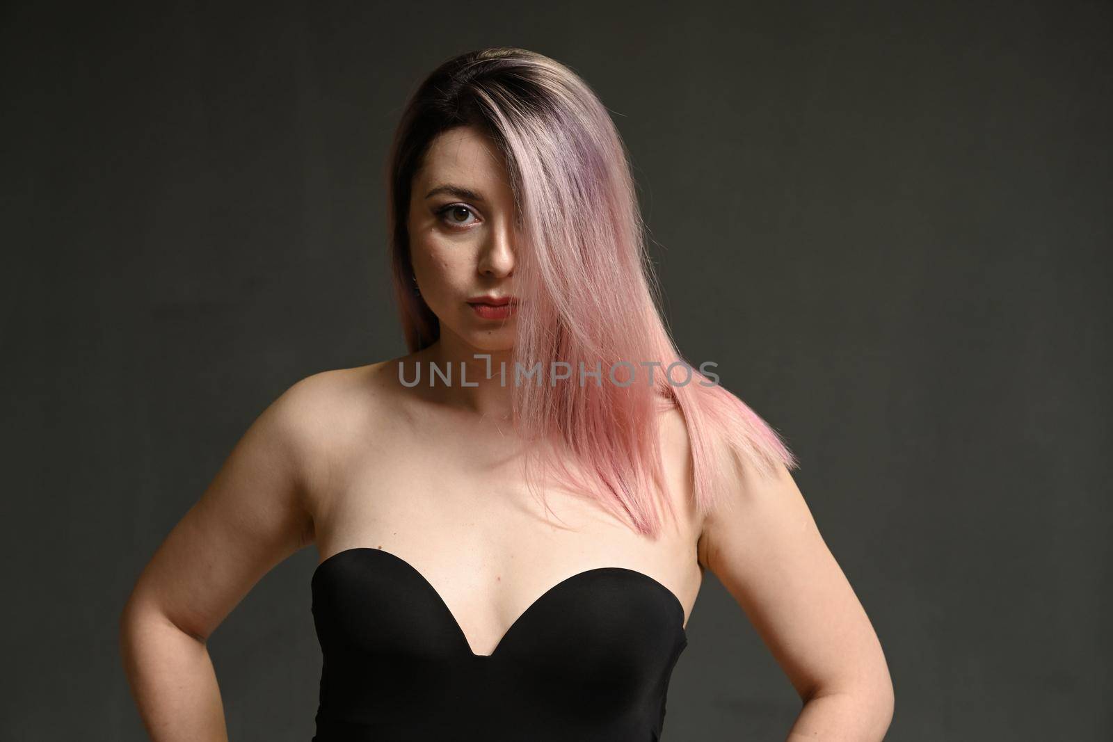 Portrait of a serious model with dyed hair and makeup looks at the camera on a gray background by chichaevstudio