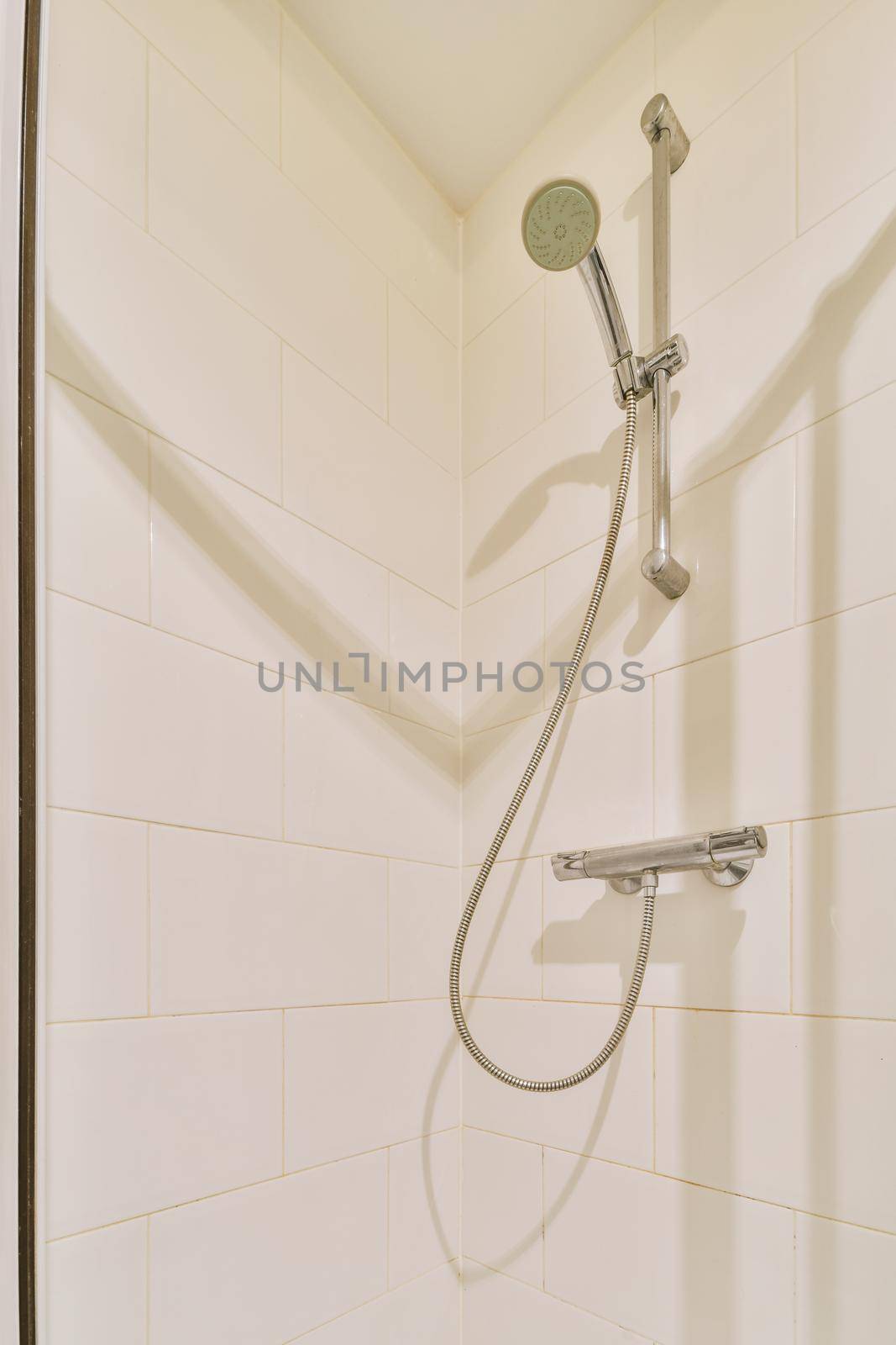 Bathtub with glass shower placed in corner near sink and mirror in small light bathroom with white tile walls