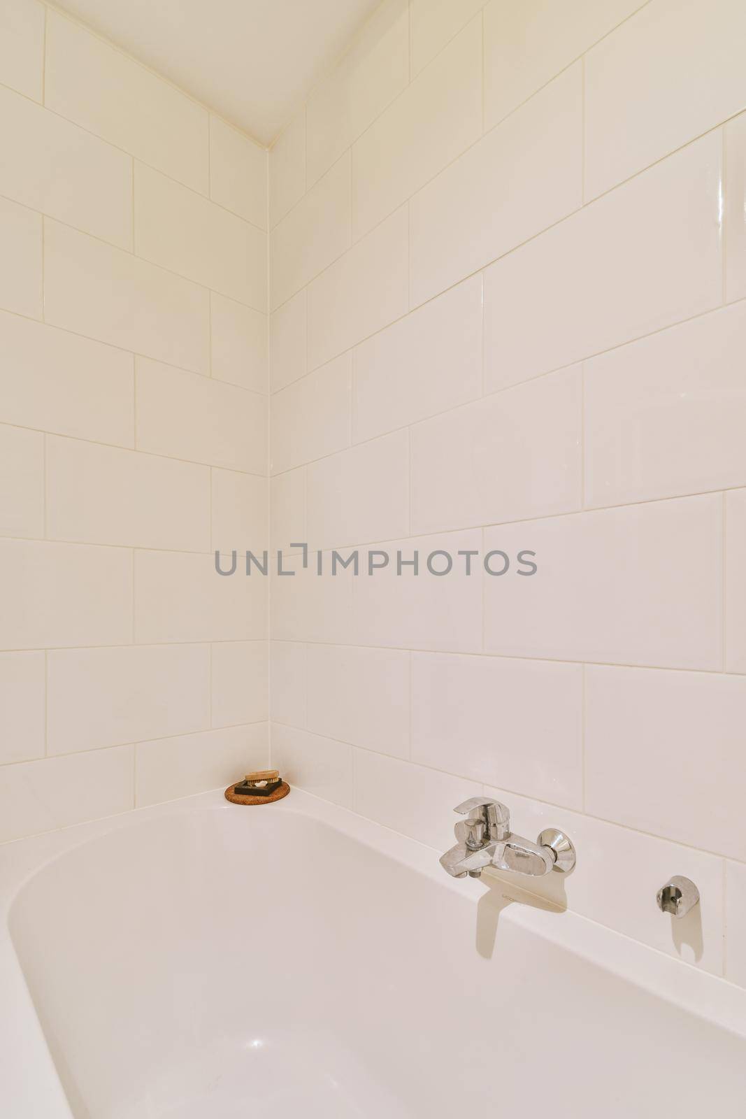 Bathtub with glass shower placed in corner near sink and mirror in small light bathroom with white tile walls