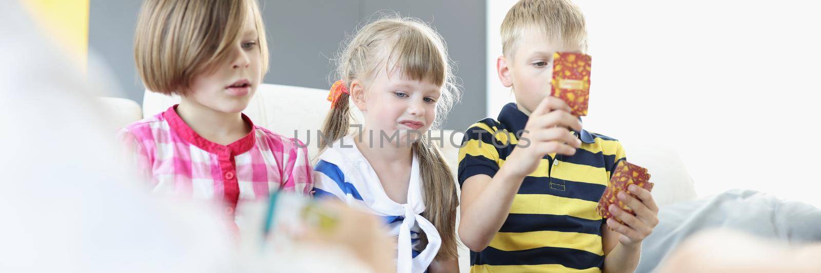 Portrait of kids sitting on couch and playing card game collectively. Brother and sister spend time together on holiday at home. Weekend, childhood concept