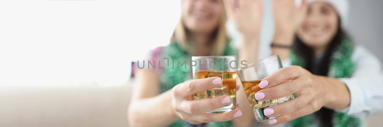 Close-up of best friends do clink with glasses filled with champagne. Happy women wave with hand and congratulate with new year. Home party, fun concept