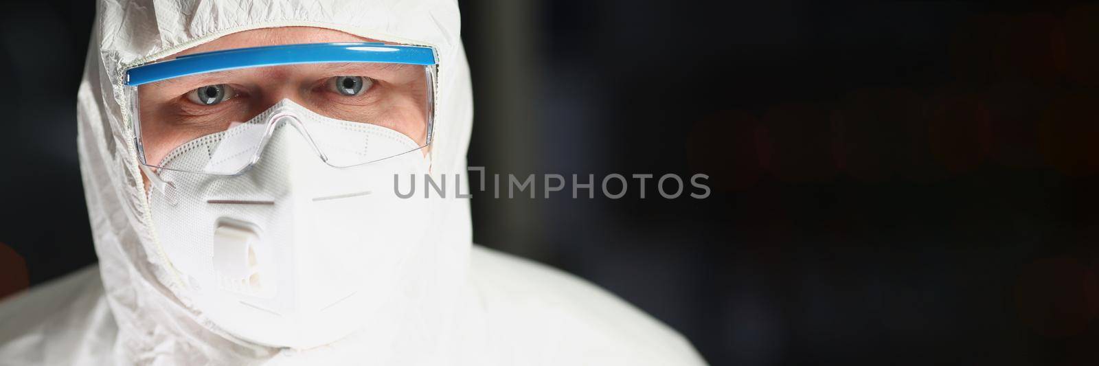 Portrait of worker in protective respirator and white coverall analyzing science experiment. Male chemist in eyeglasses work on research. Science concept