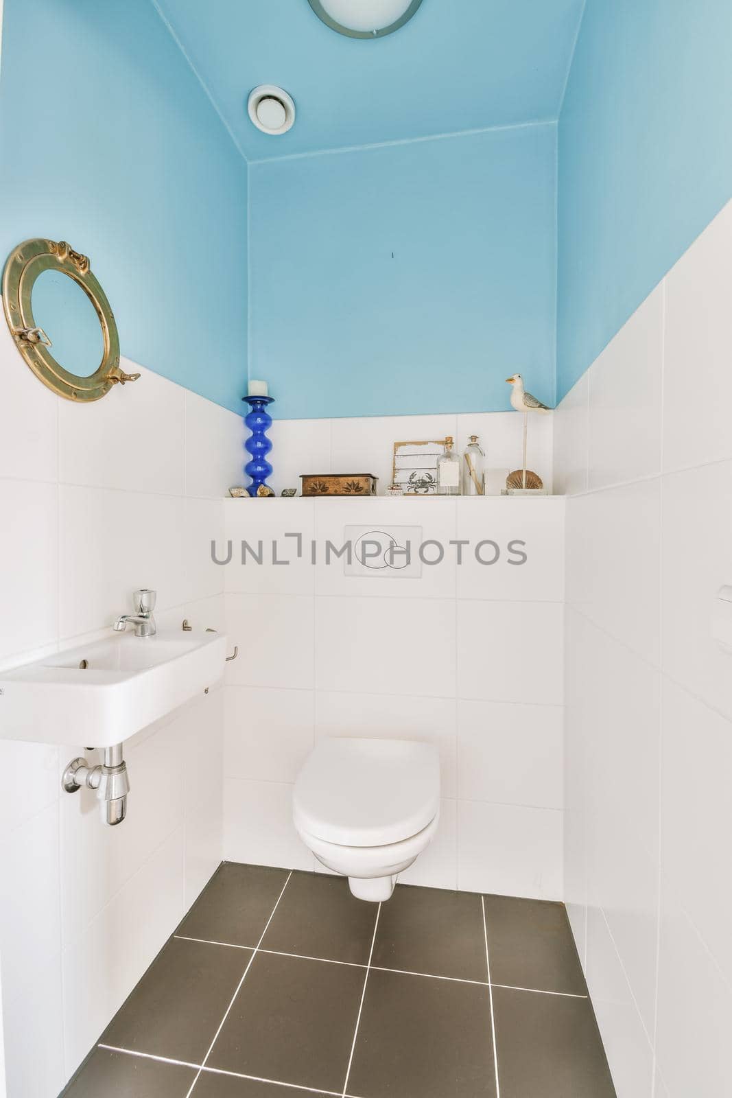 Wall hung toilet and small sink in corner in lavatory room with beige tile