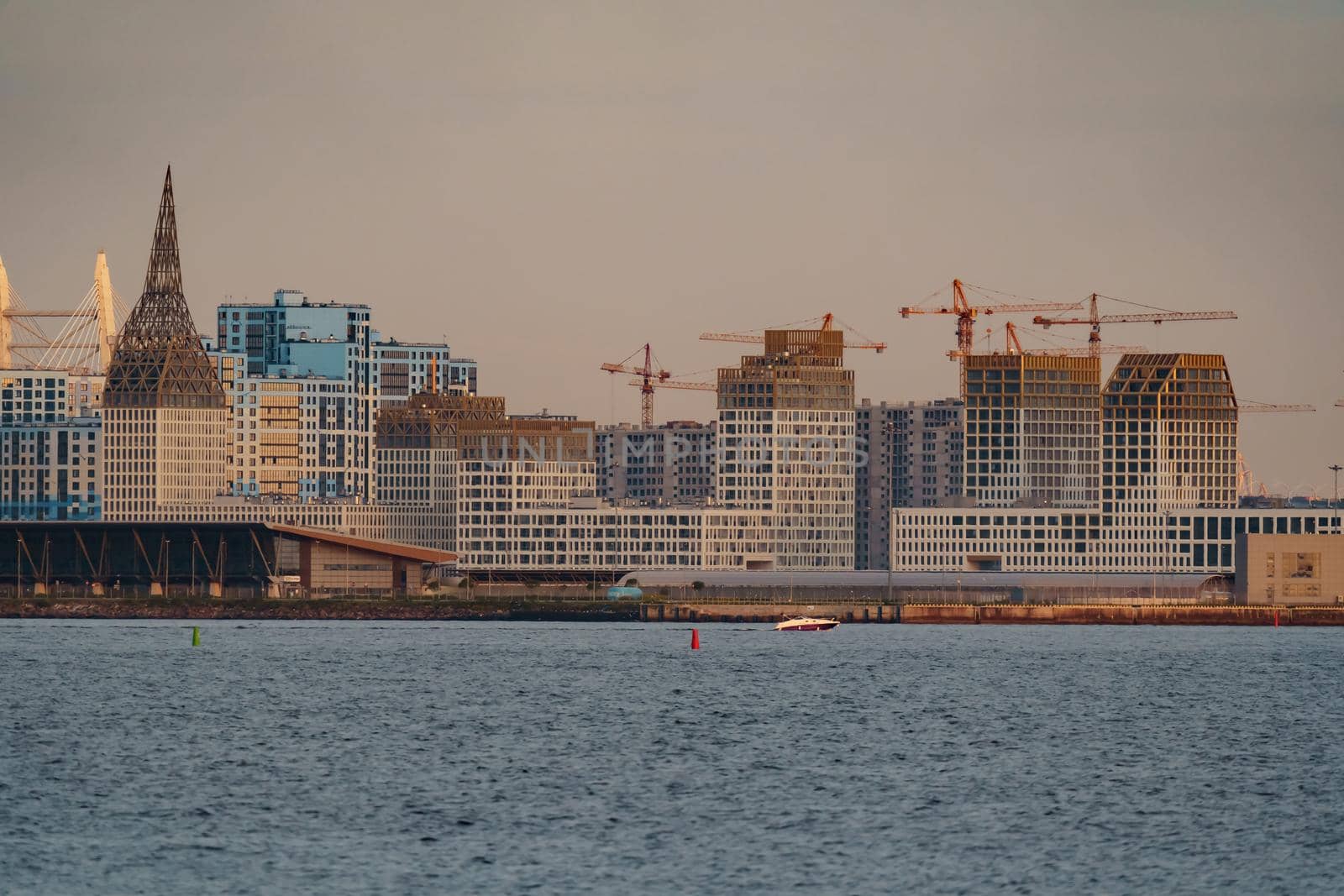 The residential complex under construction on the embankment of the Neva River on Vasilievsky island in sunset, bulk island, construction cranes. High quality photo