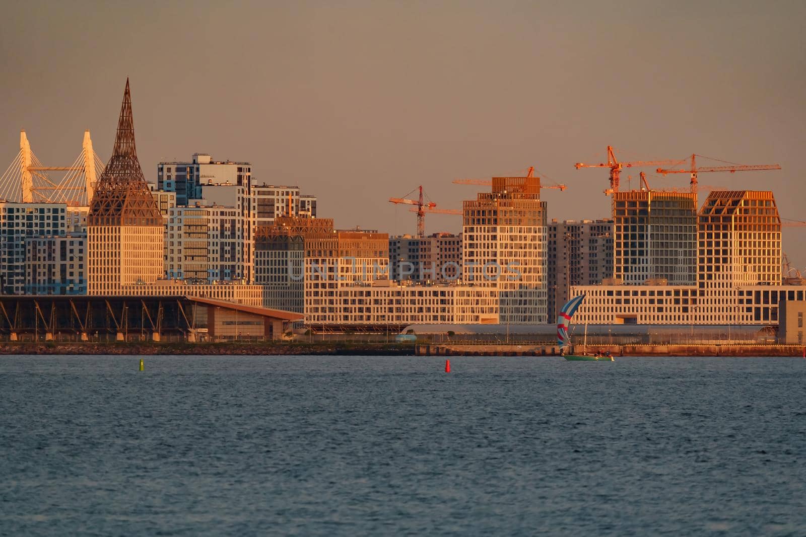 The residential complex under construction on the embankment of the Neva River on Vasilievsky island in sunset, bulk island, construction cranes. High quality photo