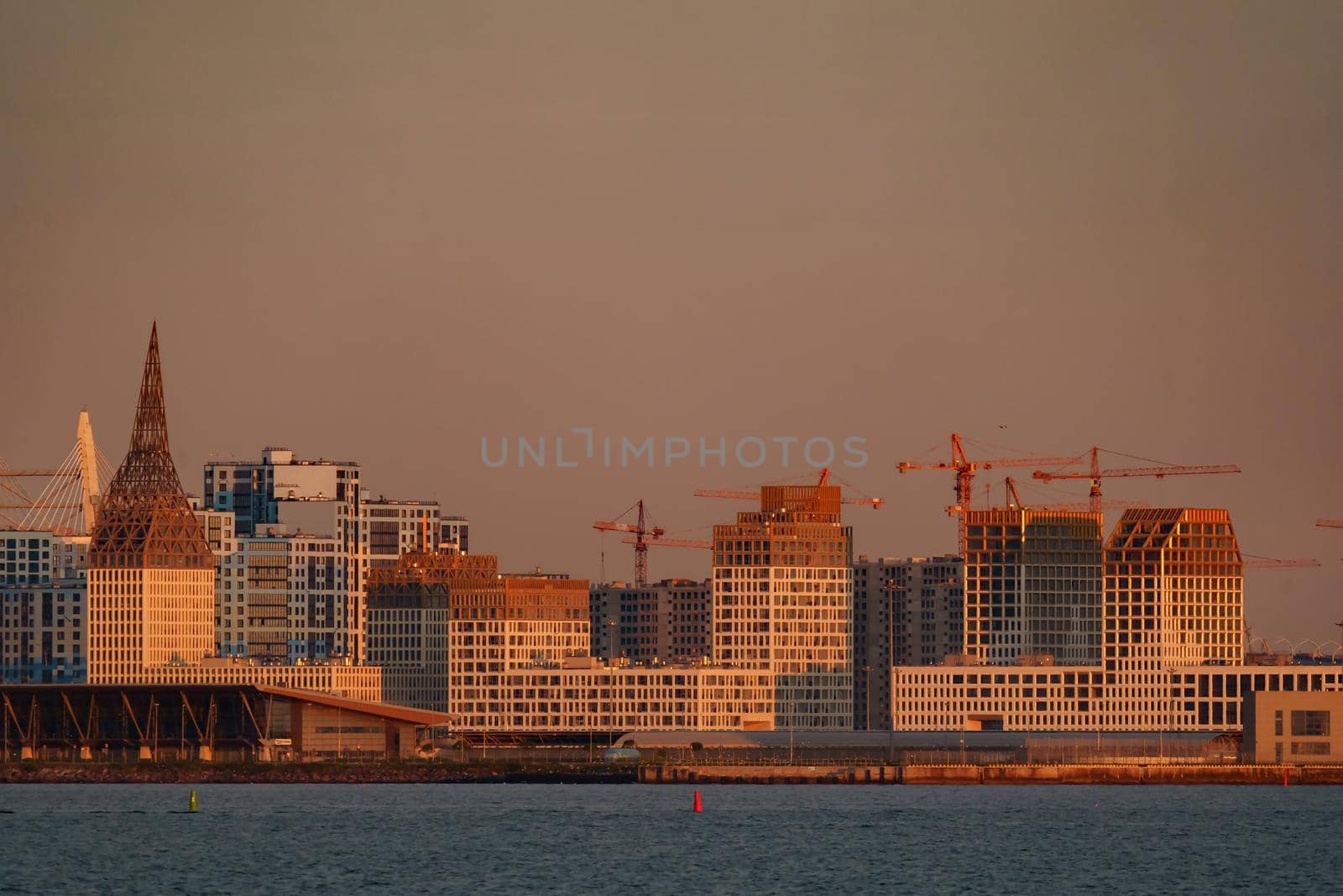 The residential complex under construction on the embankment of the Neva River on Vasilievsky island in sunset, bulk island, construction cranes. High quality photo
