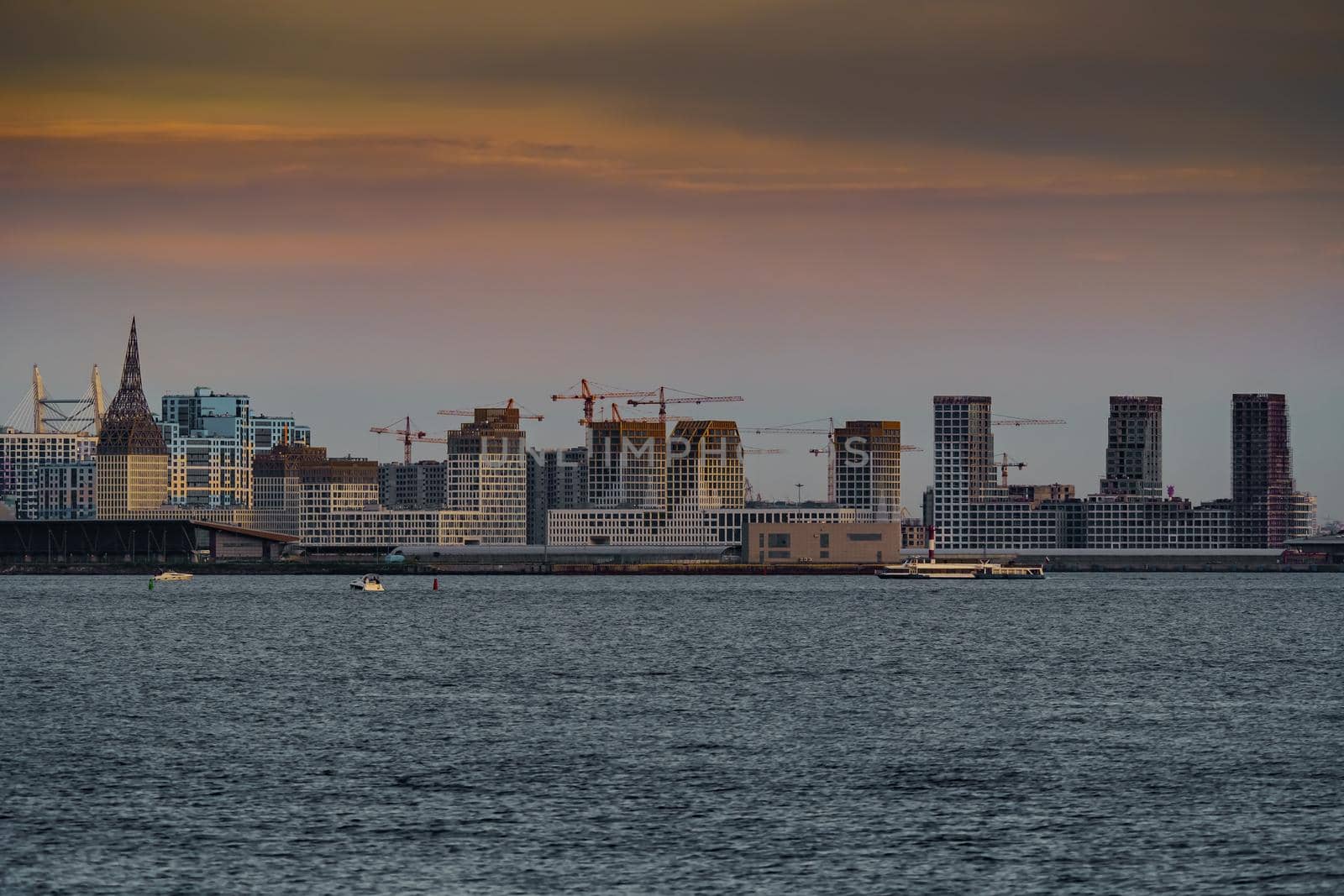 The residential complex under construction on the embankment of the Neva River on Vasilievsky island in sunset, bulk island, construction cranes. High quality photo