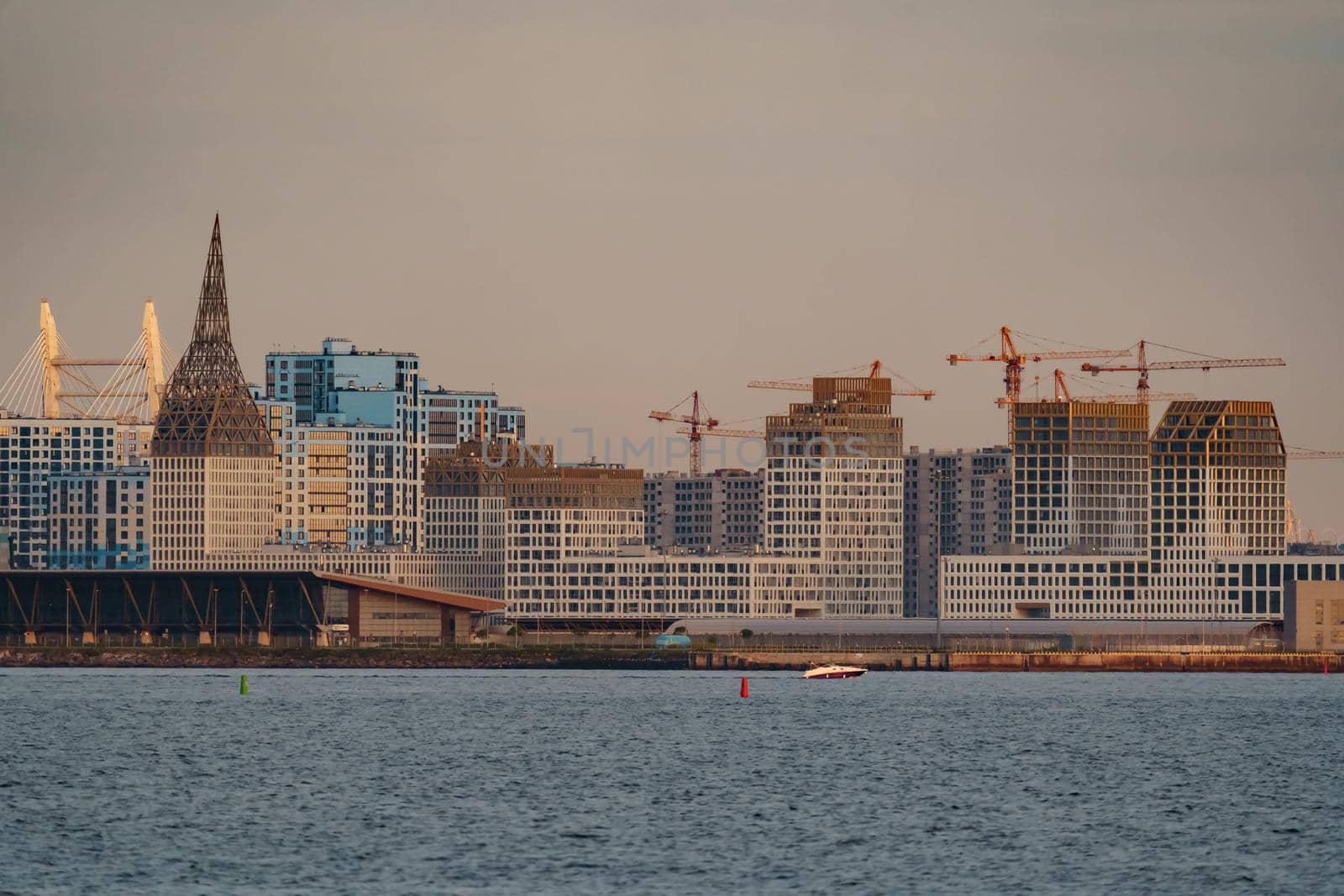 The residential complex under construction on the embankment of the Neva River on Vasilievsky island in sunset, bulk island, construction cranes. High quality photo