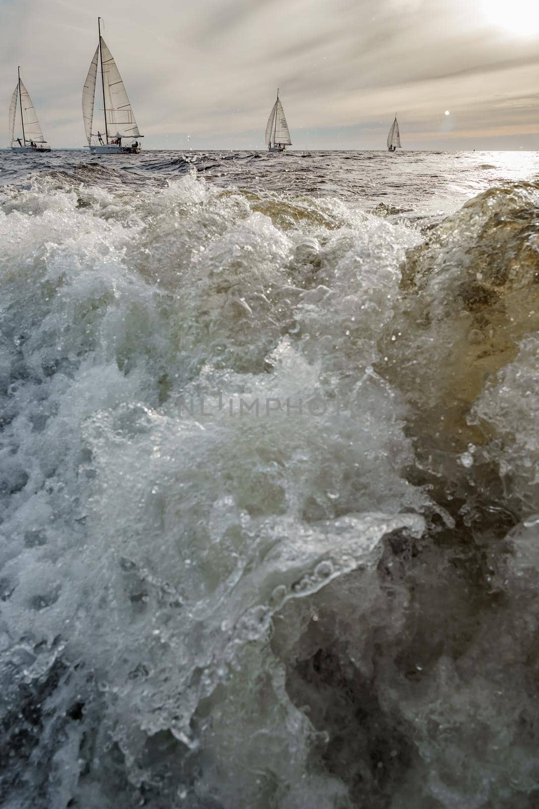 Splashes water of motor boat in the foreground, sailing yachts at sunset in background, sail regatta, big waves. High quality photo