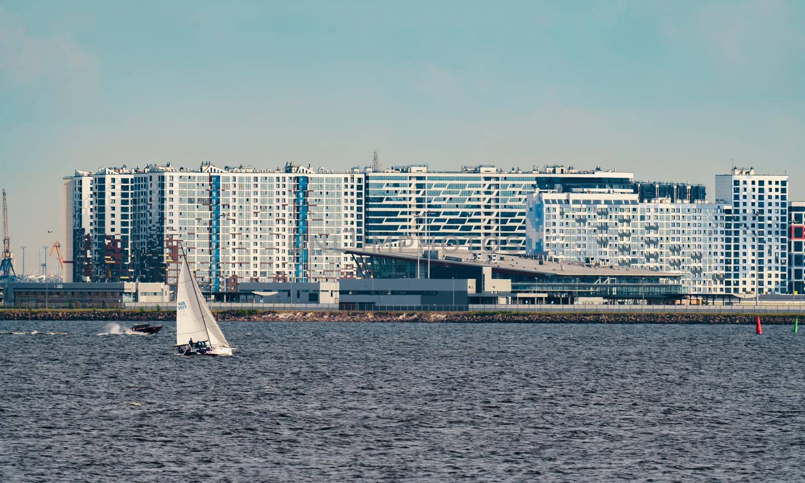 Russia, St. Petersburg, 10 June 2022: The residential complex under construction on the embankment of the Neva River on Vasilievsky island in sunny day, construction cranes, sailing yachts. High quality photo