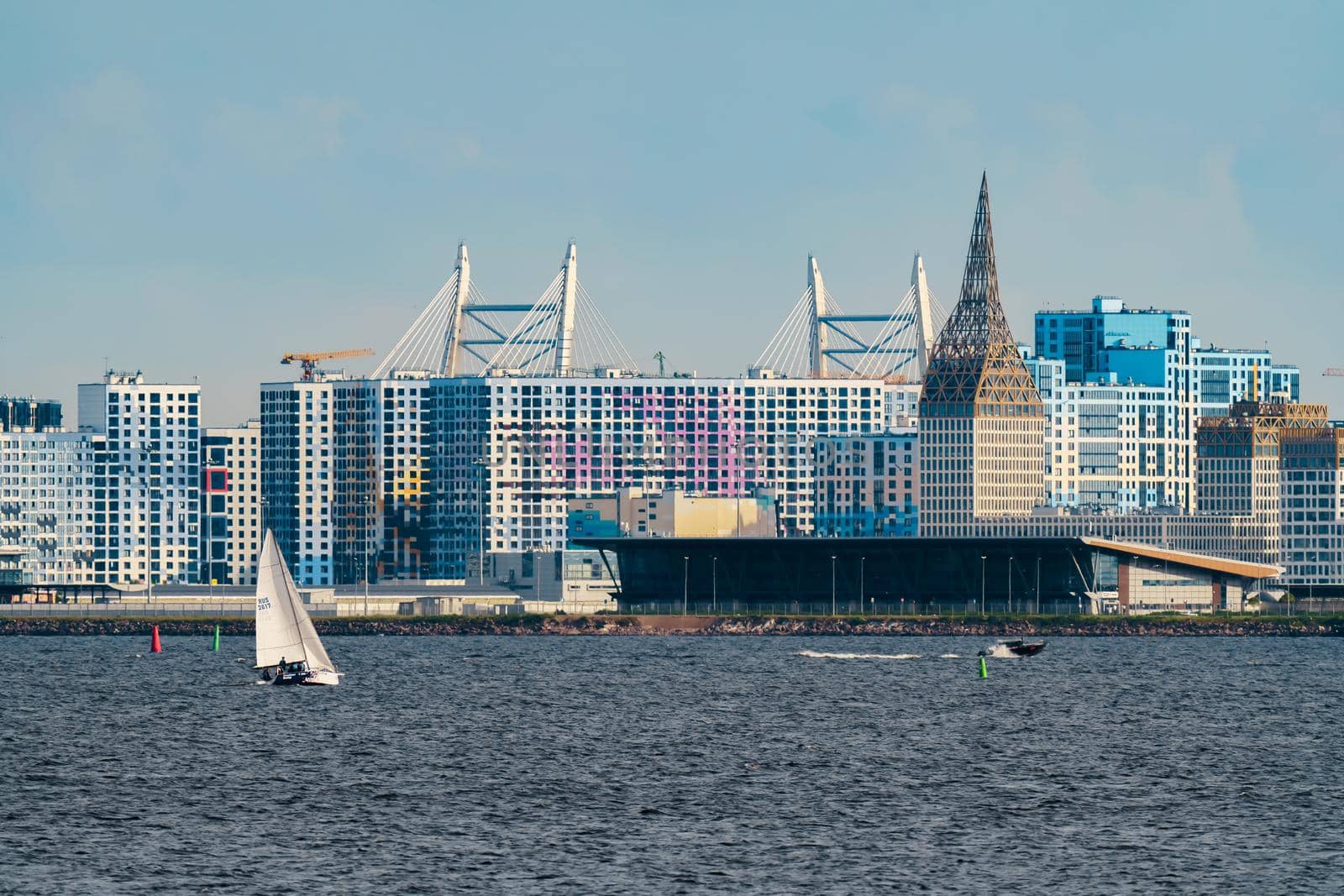 Russia, St. Petersburg, 10 June 2022: The residential complex under construction on the embankment of the Neva River on Vasilievsky island in sunny day, construction cranes, sailing yachts. High quality photo