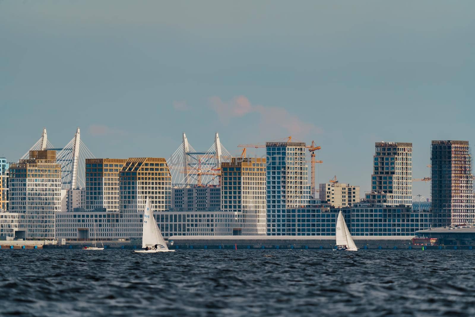 Russia, St. Petersburg, 10 June 2022: The residential complex under construction on the embankment of the Neva River on Vasilievsky island in sunny day, construction cranes, sailing yachts. High quality photo