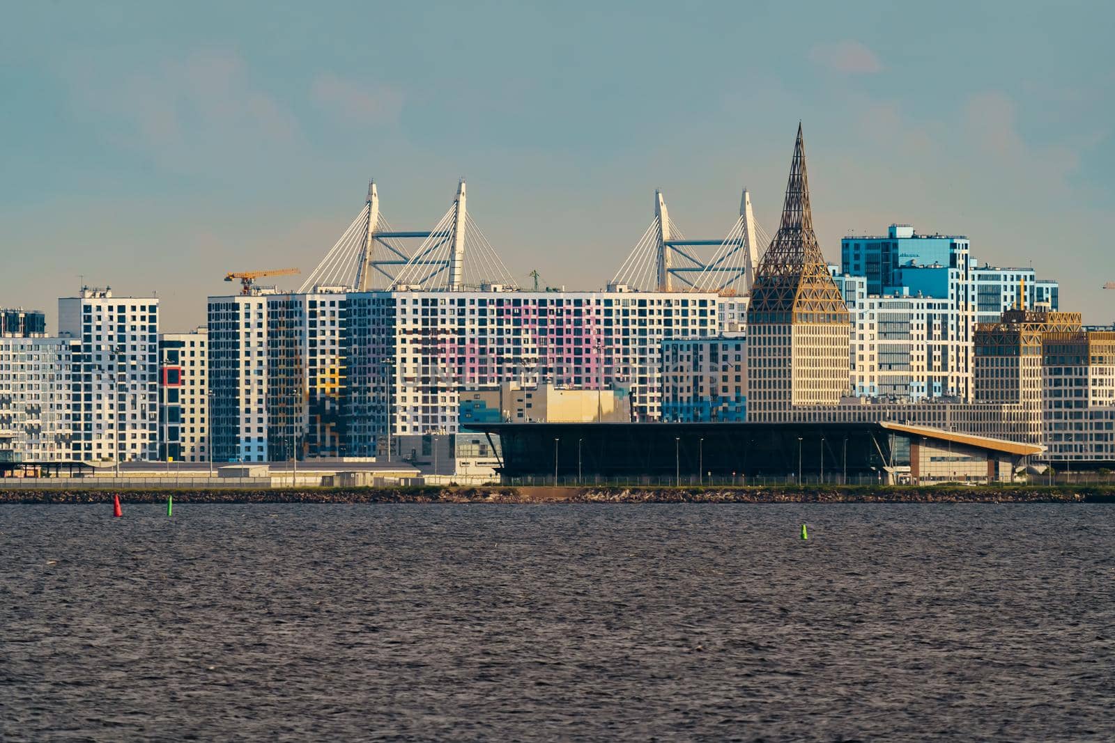 The residential complex under construction on the embankment of the Neva River on Vasilievsky island in sunny day, bulk island, construction cranes, sailing yachts, river navigation. High quality photo