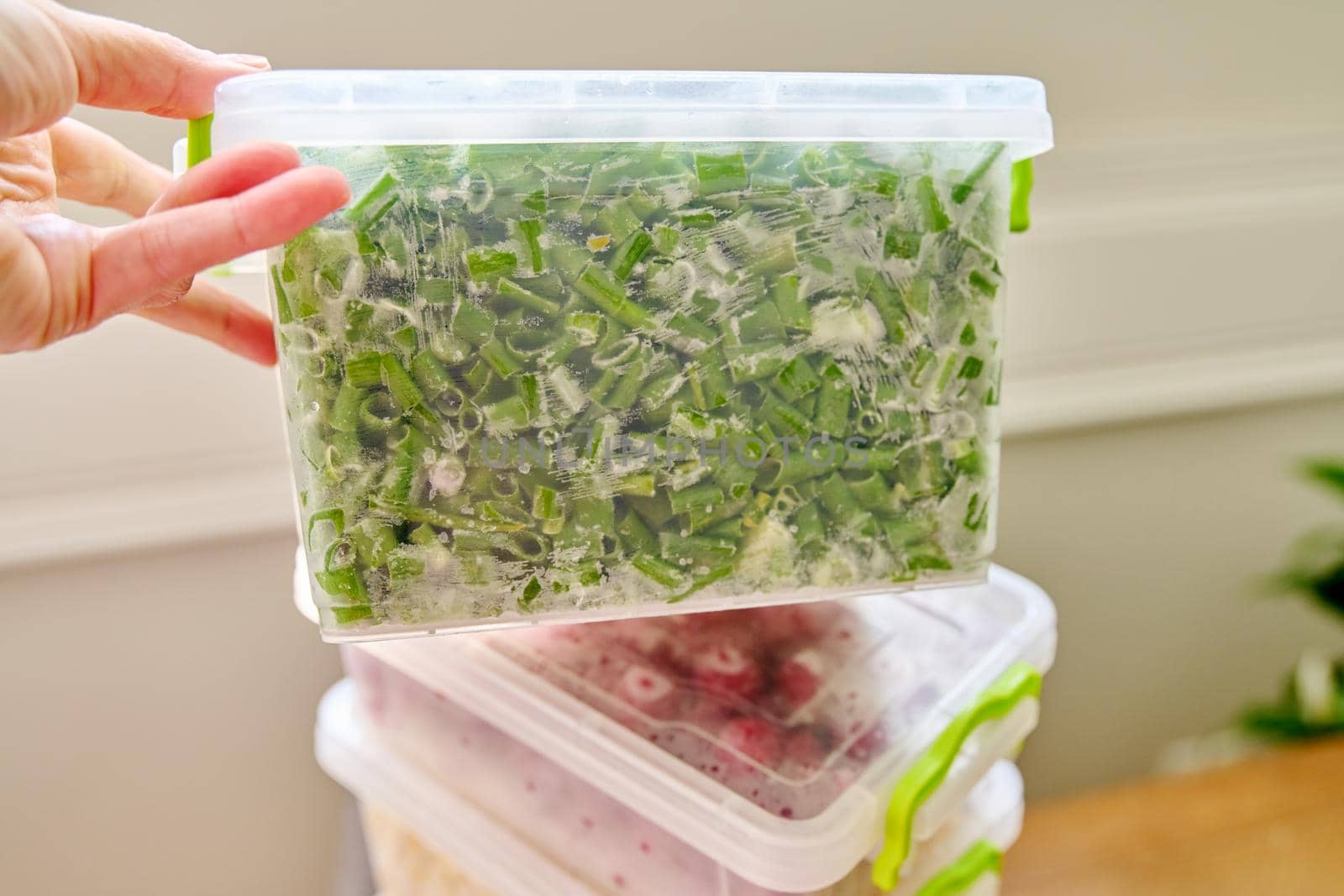 Frozen vegetables and fruits, close-up frozen in the freezer green onions in plastic containers. Seasonal vegetables, food preparations for the winter