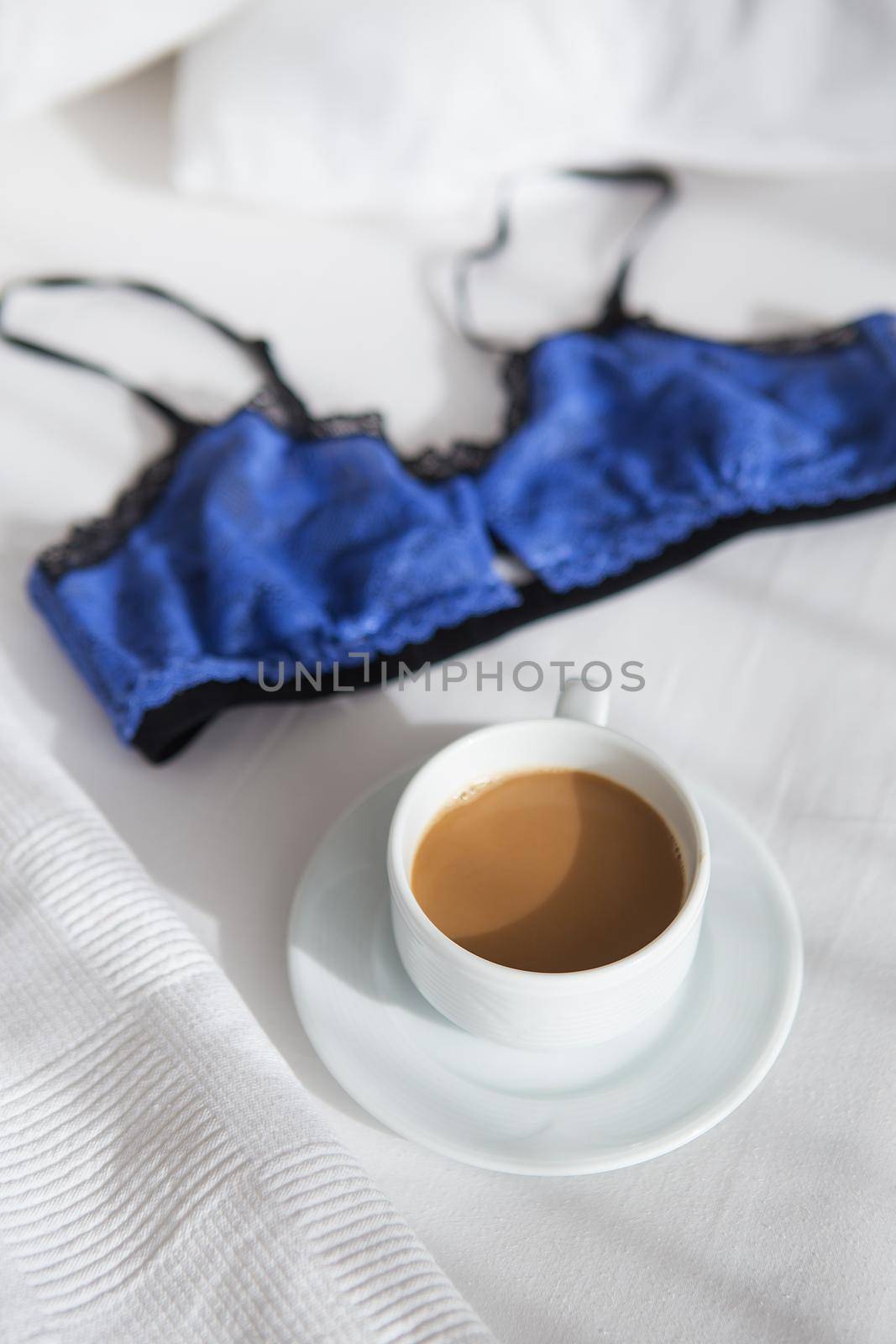 cup of coffee and a beautiful bra on a white bed by sfinks