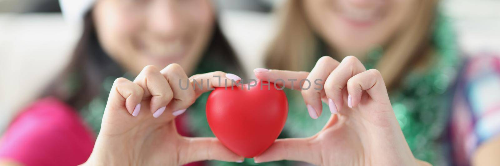 Sisters holding plastic red heart in hands and smiling by kuprevich