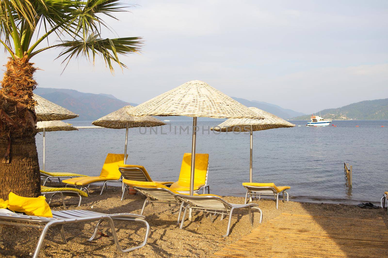 Beautiful yellow chaise lounges and umbrellas made from straw on the beach of Marmaris by sfinks