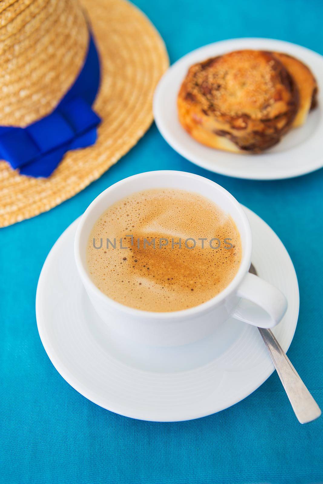 straw hat with blue ribbon, coffee and cinnamon roll on the table