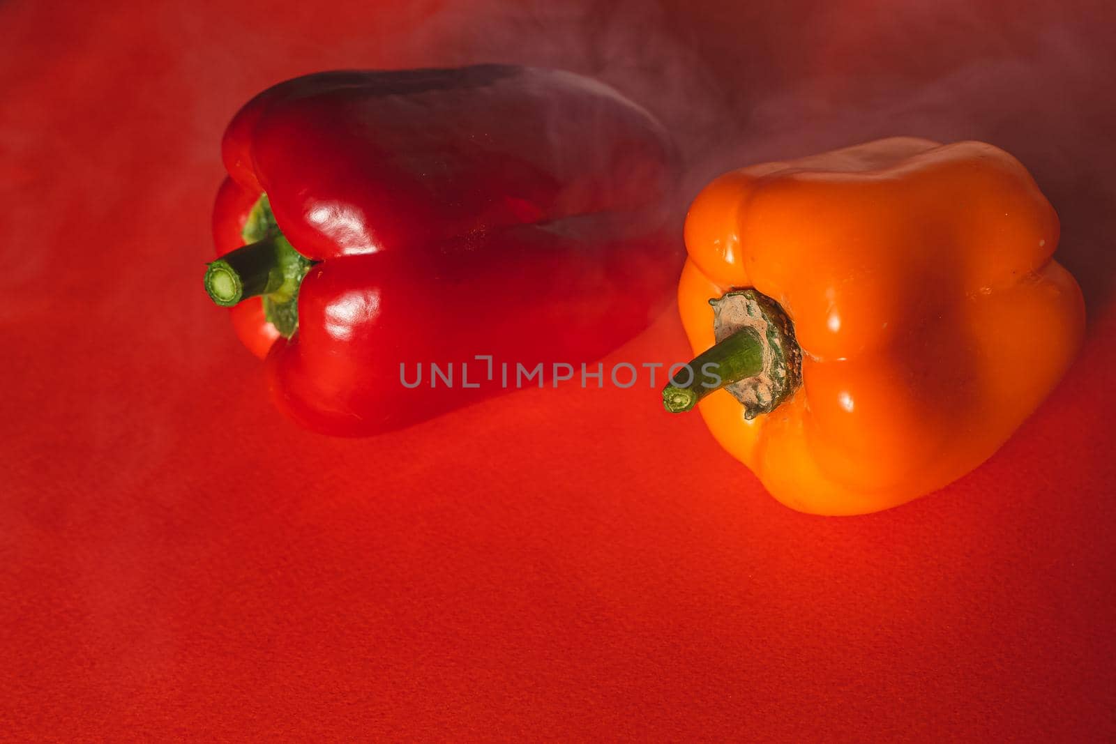 SWEET RED AND ORANGE PEPPERS ON A RED BACKGROUND WITH A LIGHT SMOKE.