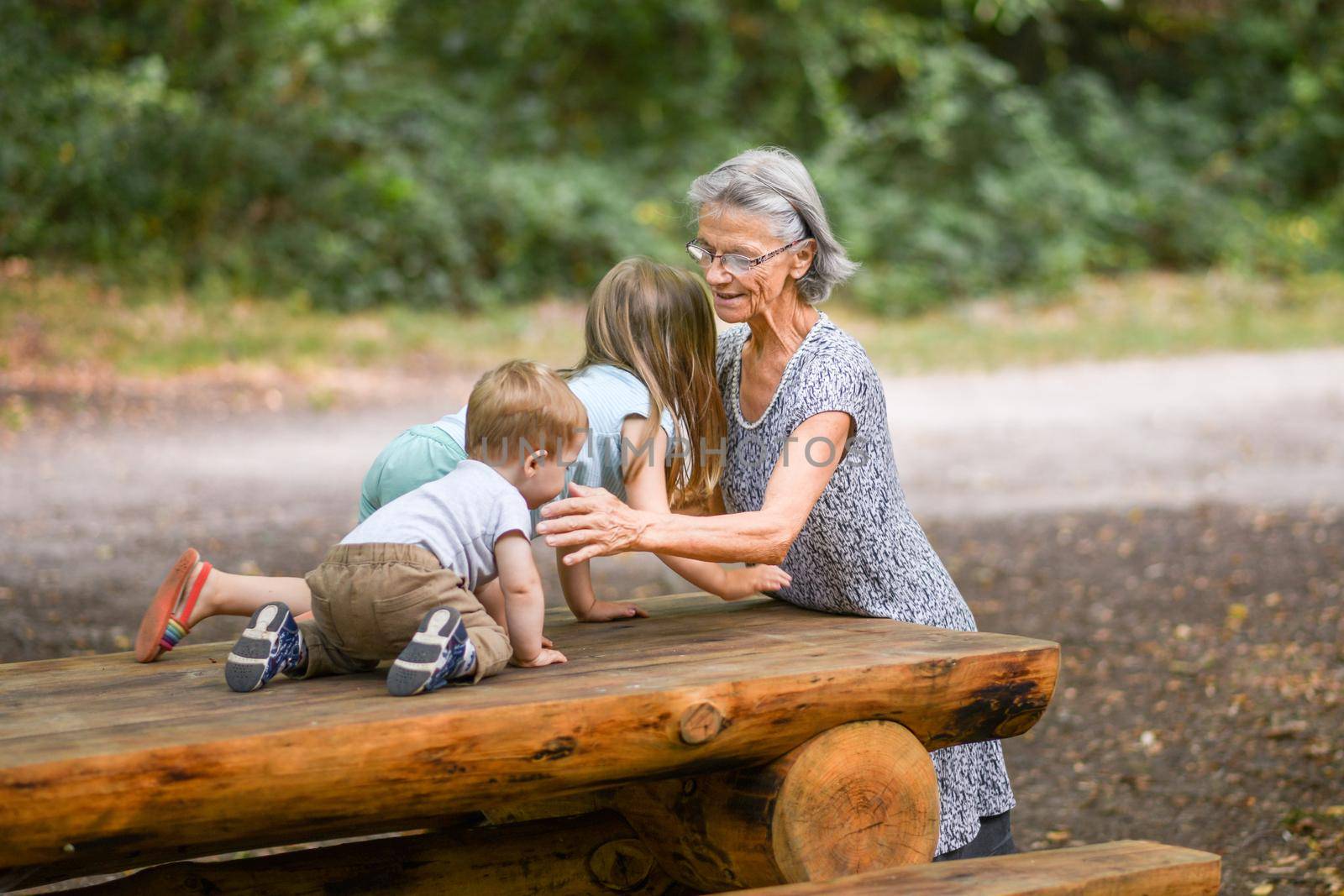 Gray-haired grandmother and her grandchildren play in the forest in summer by Godi