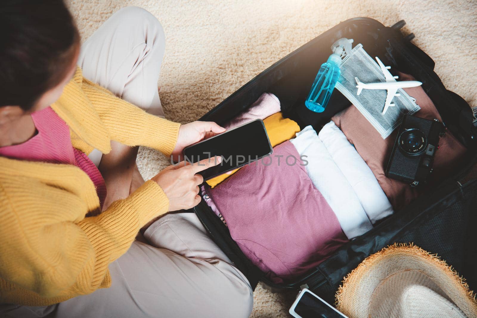 Woman using smartphone blank screen and packing suitcase bag for travel trip weekend vacation at home, female check information in tourism website on mobile phone before go to airport