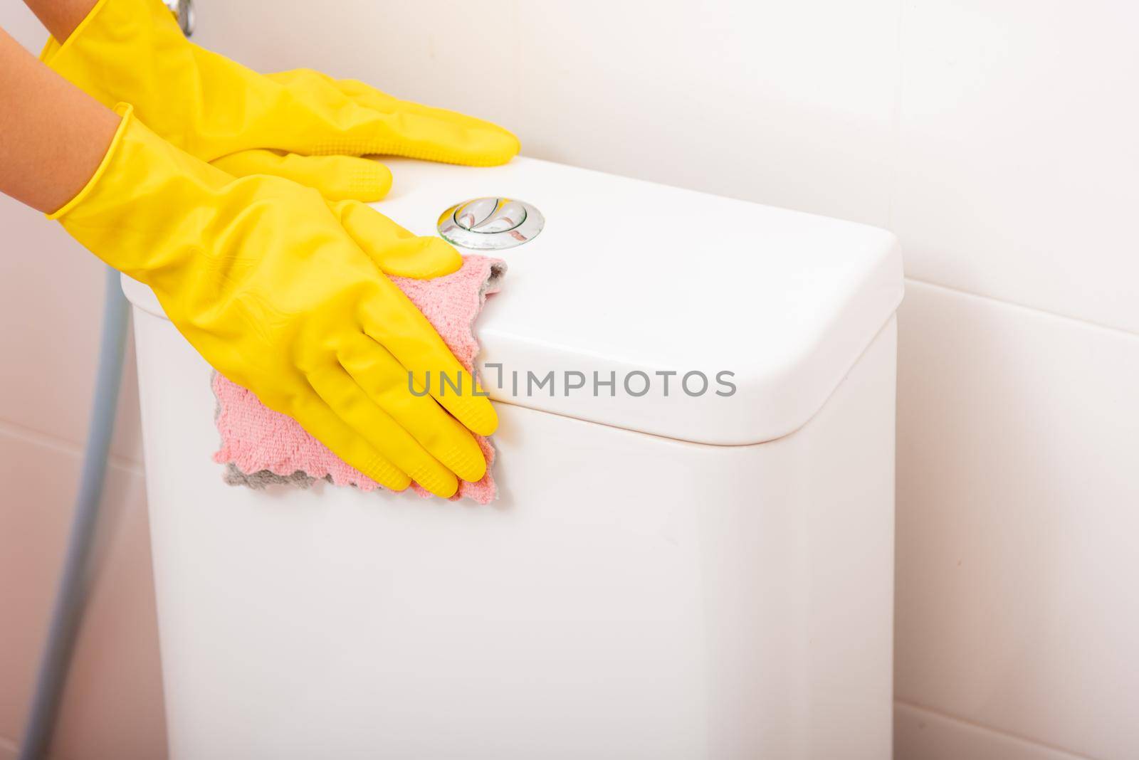 Hands of Asian woman cleaning toilet seat by pink cloth wipe restroom at house, female wearing yellow rubber gloves she sitting and cleanup or washing bathroom, Housekeeper healthcare concept