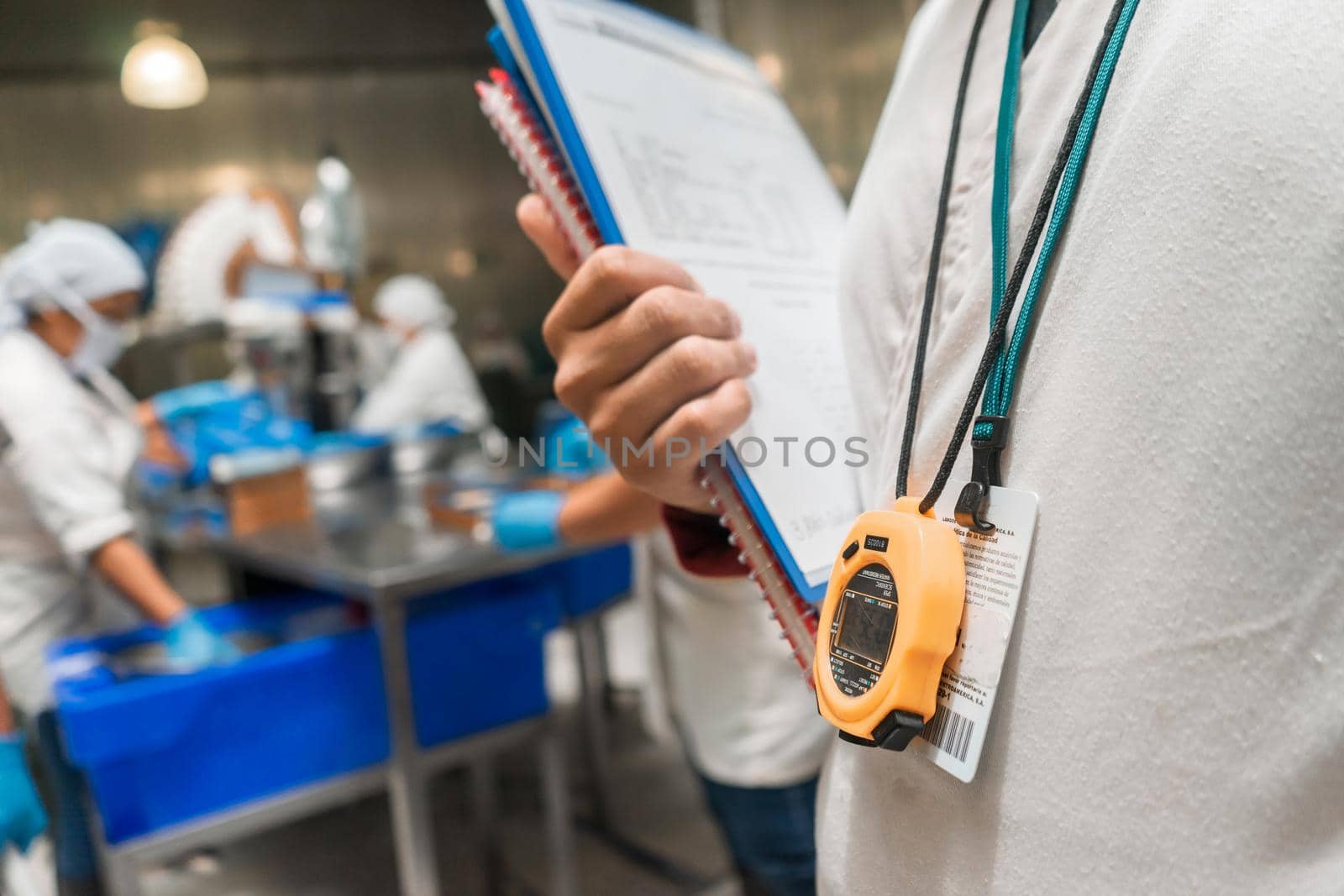 Unrecognizable inspector in an industrial food processing plant holding documents in his hands and a stopwatch around his neck in Chinandega, Nicaragua