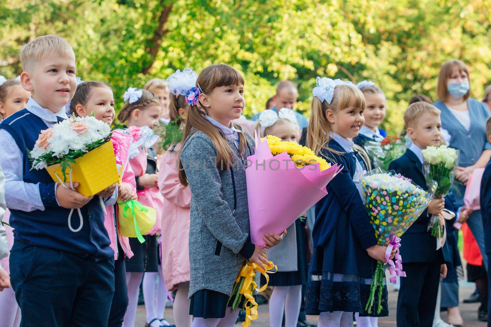 NOVOKUZNETSK, KEMEROVO REGION, RUSSIA - SEP, 1, 2021: Meeting with the first-grade pupils and teacher at schoolyard. The day of knowledge in Russia.