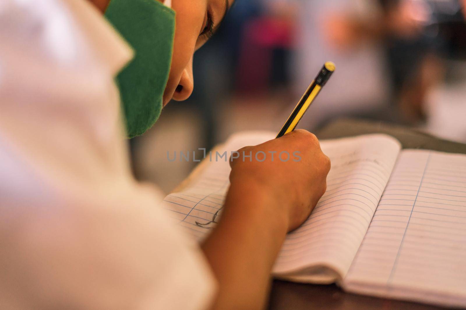 Nicaraguan boy with medical mask writing on his notebook at a desk by cfalvarez