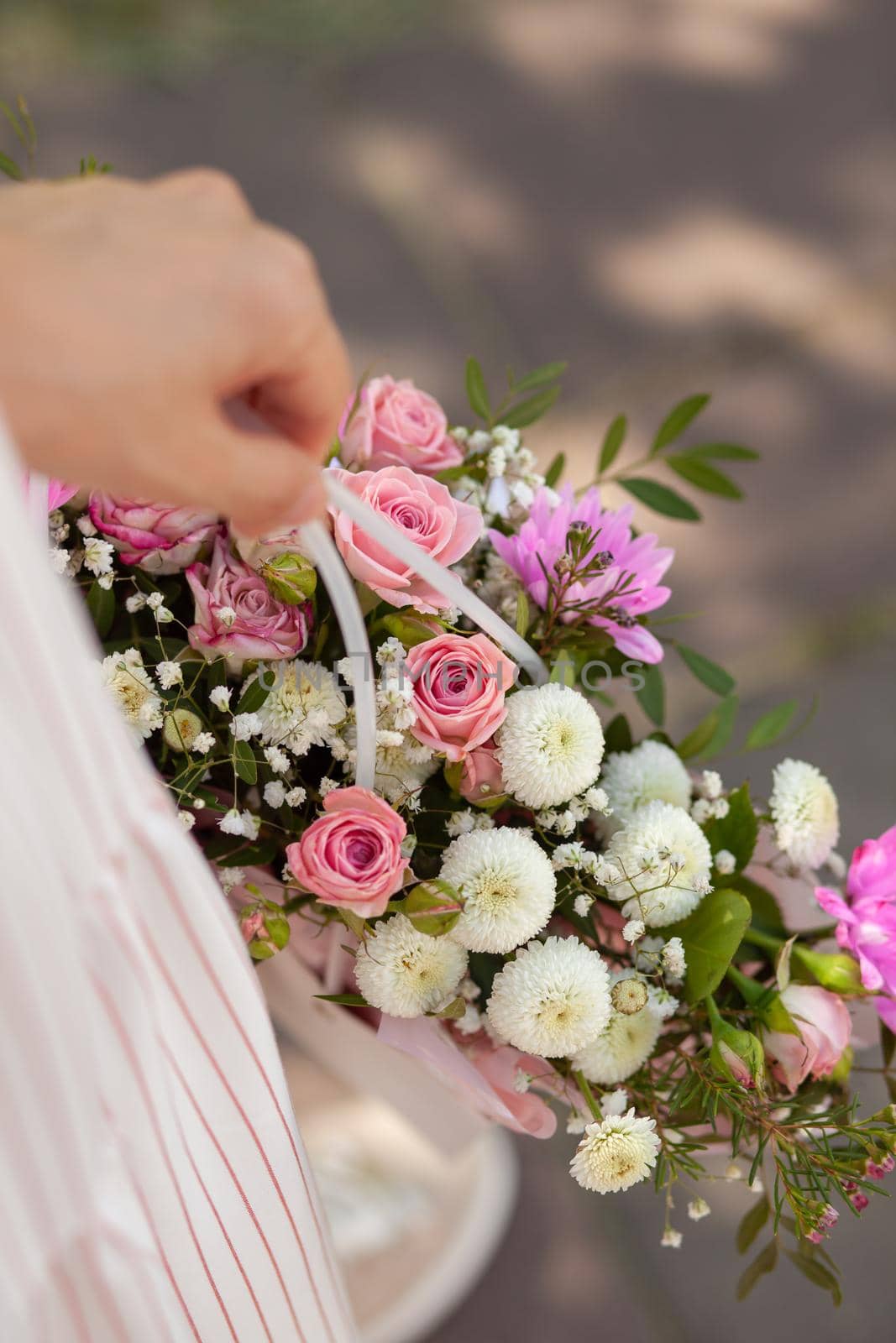 A beautiful bouquet of flowers in a box in the hands of a beautiful girl who walks along the street on a sunny day. Girl in a dress, glasses and sneakers. Focus on the background of flowers.