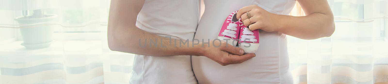 Pregnant woman and man hug belly and hold baby shoes. Selective focus. by yanadjana